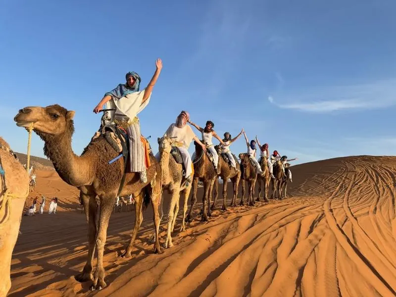 Berber guide in a blue robe walking with his camels on Sunset Camel Trek in Merzouga